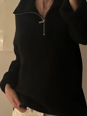 Svart stickad tröja med half zip - Snygg svart stickad tröja med halv dragkedja och hög krage. Modellen är loose fit med långa ärmar och ribbad struktur. 