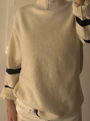 Beige polotröja med svarta ränder - Säljer en beige stickad polotröja med svarta ränder på ärmarna och nederkanten. Inköp H&M 