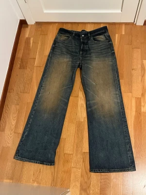 Acne Studios 2021m - Säljer ett par blå jeans från Acne Studios med breda ben och klassisk femficksdesign. Jeansen har en mörk tvätt med ljusare slitningar framtill och bak, samt en rosa patch med Acne Studios-logga bak i midjan. Materialet är robust denim i bomull.