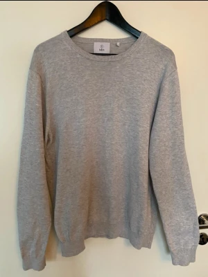 Grå pullover tröja från Bläck - Säljer en enkel och stilren grå stickad tröja från Bläck i storlek L. Tröjan har rund hals, långa ärmar och ribbade muddar vid hals, ärmslut och nederkant. Perfekt för lager-på-lager och chill dagar. Materialet är mjukt och skönt stickat.