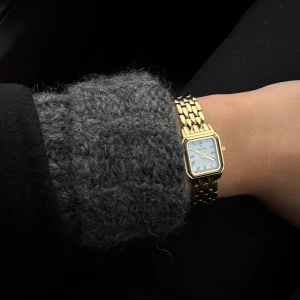Guldfärgad klocka från Mockberg - Snygg guldfärgad klocka från Mockberg med fyrkantig vit urtavla och länkarmband i metall. Klockan har en stilren design med tunna svarta markeringar och klassisk känsla. Perfekt accessoar för dig som gillar tidlös stil. 