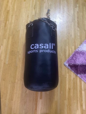 Svart träningsväst från Casall - Säljer en svart träningsväst från Casall med sportig look och tydlig logga framtill. Västen har en rund form och är tillverkad i slitstark syntet med metallkedjor för upphängning. Perfekt för dig som vill ha en cool och funktionell väst till gymmet.