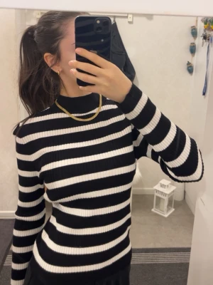 Svartvit randig ribbad polotröja - Säljer en svartvit randig tröja med ribbad struktur. Tröjan har lång ärm och en hög krage som ger en snygg och modern look. Perfekt att styla med jeans eller kjol för en cool vibe. Materialet känns mjukt och stretchigt mot kroppen. Storleken är XS
