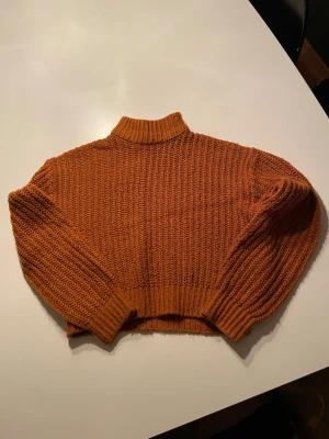 Stickad orange tröja från DIVIDED - Säljer en snygg stickad tröja från DIVIDED i storlek XS. Tröjan är orange, har en ribbad hög hals och långa ärmar med breda muddar. Modellen är croppad och har en chunky stickning som ger en cool och avslappnad vibe.