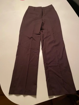 Bruna kostymbyxor från BikBok - Snygga bruna kostymbyxor från BikBok i storlek 34. Byxorna har en rak och lite vidare passform med hög midja. Perfekt för dig som gillar stilrena och klassiska byxor.