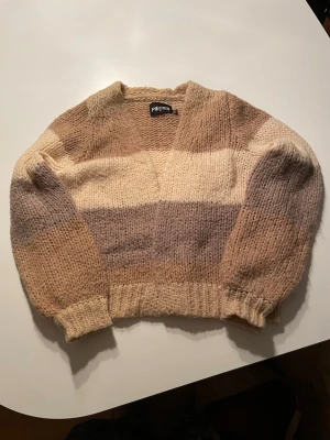 Randig stickad kofta från Pieces XS - Mysig stickad kofta från Pieces i storlek XS. Koftan har breda ränder i beige, brun toner, med en croppad passform och ribbade muddar. Perfekt för lager på lager under höst och vinter. 