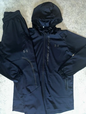 UNDER ARMOUR STORM TRACKSUIT - UNDER ARMOUR STORM TRACKSUIT- svart och blå   Sitter riktigt snyggt på kroppen och materialet är stretchigt/bekvämt