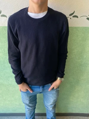 Mörkblå stickad tröja från Riley - Snygg mörkblå stickad tröja från Riley med rund hals och långa ärmar. Enkel och stilren design som passar perfekt till jeans eller chinos. Mjukt material som känns skönt mot huden och ger en avslappnad look.