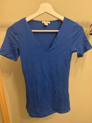 Blå v-ringad topp från Amisu XS - En enkel och stilren blå topp från Amisu i storlek XS. Toppen har korta ärmar och en djup v-ringning framtill. Tillverkad i mjukt material som känns skönt mot huden. Aldrig använd❤️