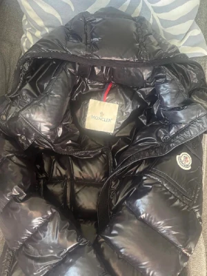 Svart dunjacka från Moncler med bälte - Moncler Grenadille-dunjacka i svart. Köpt från Von Greven Closet, en välkänd och pålitlig återförsäljare. Storlek XS/S. Jackan är i gott skick med normala tecken på användning. Har ett bälte i midjan ej avtagbar. 