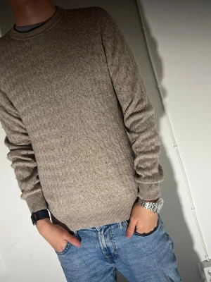 Beige stickad tröja från MNG Man - Säljer en beige stickad tröja från MNG Man med diskret mönster och rund hals. Tröjan har långärmade ärmar och ribbade muddar. Materialet är en mix av polyamid, viskos, ull och kashmir vilket gör den mjuk och skön. Perfekt till jeans för en chill look.