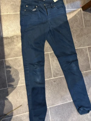 Blå skinny jeans Gemma Denim W25 - Säljer ett par blå skinny jeans från Gemma Denim i storlek W25. Jeansen har klassisk femficksdesign, dragkedja och knapp framtill. Materialet är mjukt och stretchigt jeans, perfekt för dig som gillar en tight passform och stilren look.