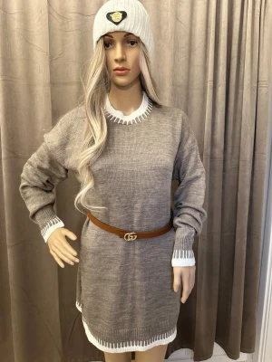 Beige stickad lång tröja med vita detaljer - Snygg beige stickad lång tröja med vita ribbade detaljer vid hals, ärmslut och nederkant. Tröjan har en relaxed passform och långa ärmar, perfekt att styla med bälte i midjan för en trendig look.