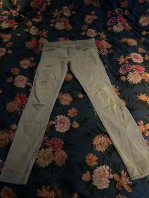 desquared ljusgrå jeans med slitningar.    - Säljer ett par ljusgrå jeans från desquared med skinny passform. Jeansen har flera slitningar och hål på framsidan samt klassiska fem fickor och bälteshällor. Materialet är jeans och de har en snygg, urban vibe med detaljerade sömmar. Passar dig som är mellan 180-185cm lång 
