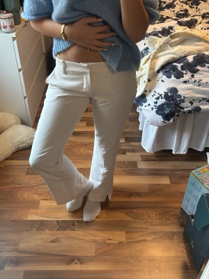 Vita låg midjade bootcut byxor med slits från Bikbok - Snygga vita lågmidjade bootcut byxor med slits vid benslut. Byxorna har låg midja och är tillverkade i ett mjukt bomullsmaterial. De har klassisk knäppning framtill och en clean look utan synliga detaljer. Perfekta för dig som gillar stilrena och trendiga plagg. I storleken 38 men passar mig som har 36