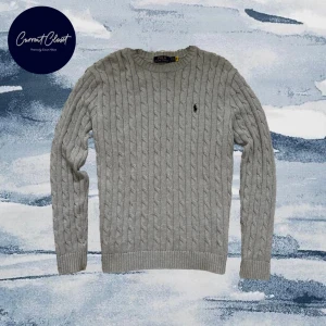 Grå kabelstickad tröja Polo Ralph Lauren - Snygg grå kabelstickad tröja från Polo Ralph Lauren med klassisk rund hals och svart broderad logga på bröstet | Size: S men passar M |