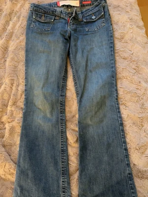 Blå bootcut jeans från Jeansshoppe - Snygga blå jeans från Jeansshoppe i bootcut-modell med stretch. Klassisk femficksdesign med knappar och dekorativa sömmar på bakfickorna. Jeansen har normal passform och är tillverkade i jeansmaterial med coola detaljer och kontrastsömmar.