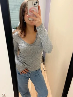 Grå v-ringad stickad tröja - Snygg grå stickad tröja med v-ringning och långa ärmar. Perfekt att matcha med jeans för en avslappnad stil. Tröjan har en mjuk känsla och sitter normalt på kroppen.