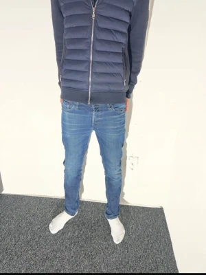 Blå skinny jeans från Jack & Jones - Säljer ett par blå skinny jeans från Jack & Jones med klassisk femficksdesign och snygga slitningar. Jeansen har låg midja och smal passform som sitter tajt längs benen. Materialet är bomull med en mjuk jeanskänsla. Perfekt för dig som gillar en modern och stilren look.