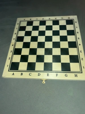 Beige och svart schackbräda i trä - Säljer ett schackspel med bräda i trä, klassiskt rutmönster i beige och svart. Brädan är vikbar med lås och kommer med schackpjäser i två färger, ljusbeige och mörkbrun, allt i trä. Perfekt för dig som gillar strategi och vill ha ett snyggt schackset hemma.