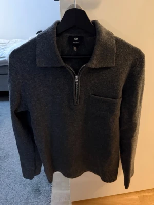 Grå stickad halfzip  - Mörkgrå stickad tröja från H&M i storlek XS med krage och half zip framtill. Regular fit och långärmad modell, perfekt för kyliga dagar. Tröjan har en enkel bröstficka och ribbade muddar vid ärmslut och nederkant. Snygg och stilren för en chill look.