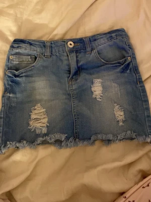 Blå jeanskjol från LAB Industries - Säljer en blå jeanskjol från LAB Industries i storlek 146. Kjolen har slitna detaljer, fransad nederkant och klassiska fickor både fram och bak. Perfekt för dig som gillar en avslappnad och cool stil.