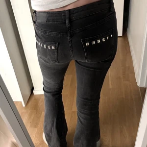Svarta bootcut jeans med nitar - Säljer ett par svarta jeans med bootcut-snitt och låg midja. Jeansen har coola silverfärgade nitar på fickorna både fram och bak, vilket ger dem en edgy vibe. Materialet är klassisk jeans och passformen är normal. Perfekta för dig som gillar detaljer och vill sticka ut.