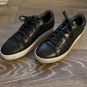 Svarta sneakers från Vagabond - Snygga svarta sneakers från Vagabond med vit platt sula och klassisk rund tå. Skorna är gjorda i skinn och har snörning framtill. Perfekta för dig som gillar stilrena och tidlösa sneakers med en clean look. Den ena skon är lite sönder som man ser på bild 4. 