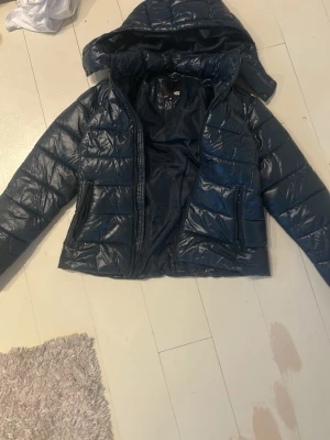 Mörkblå 157 jacka - Säljer den populära mörkblå pufferjacka från 157 i storlek XS. Andvänd några gånger men väldigt bra skick. Jackan har huva, dragkedja framtill och två sidofickor med dragkedja. Den är quiltad och har en glansig yta som ger en cool vibe. Perfekt för kalla dagar när du vill vara både varm och snygg.