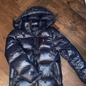 Navy blue jacka från Polo Ralph Lauren - Snygg mörkblå pufferjacka från Polo Ralph Lauren med huva och dragkedjor. Jackan är knappt använd och har inga fläck eller hål. Köpt från själva butiken för ca 6000 kr. Pris kan diskuteras och skriv om mer bilder behövs. 