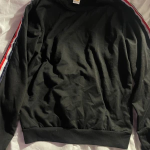 Svart sweatshirt med ränder från Liranmei - Svart sweatshirt från Liranmei med långa ärmar och coola röda, vita och blå ränder längs båda ärmarna. Tröjan har rund halsringning och är tillverkad i mjuk bomullsmix. Perfekt för en avslappnad och sportig stil.