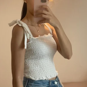  Linne med knytband - Supersöt vit linnetopp med smockad struktur och knytbara axelband. Toppen är croppad och har volangkant nedtill. Köpt från gina tricot.