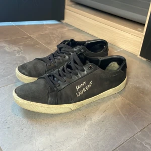 Svarta Saint Laurent sneakers - Svarta sneakers från Saint Laurent med vit sula och handskriven logga på sidan. Skorna har snörning och är tillverkade i en mix av skinn och textil. Perfekta för dig som gillar en stilren men edgy look.