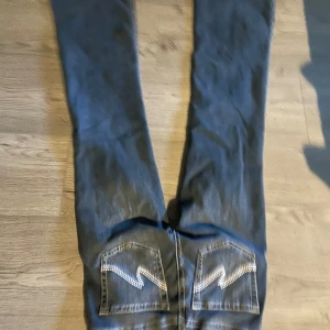 Blå bootcut jeans från Nelly - Snygga blå jeans från Nelly med bootcut-modell och coola broderade detaljer på bakfickorna. Klassisk femficksdesign och låg midja. Jeansen är i denim med kontrastsömmar och har en riktigt trendig vibe.