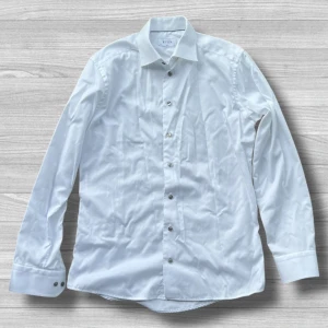 Vit slim fit skjorta från Eton - Snygg vit skjorta från Eton i slim fit-modell, perfekt för dig som gillar en stilren och klassisk look. Skjortan har långa ärmar, knappar framtill och är tillverkad i mjuk bomull. Passar dig som vill ha en fräsch och enkel stil.