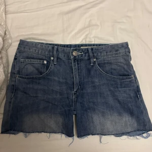 Lågmidjade jeansshorts - Säljer ett par klassiska blå jeansshorts från H&M Denim med råa, fransiga benslut och femficksmodell. Shortsen har normal passform och är tillverkade i slitstarkt jeanstyg. Perfekta för sommaren och enkla att matcha med allt. Säljer då de är lite för små och lite för långa i benen, men det går absolut att klippa om man vill ha de kortare. Skriv om ni har frågor om mått, eller vill ha bild med de på! Jag har S och jag får på mig de men de sitter lite för ditt för min smak.