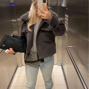 Grå kort jacka med pälskrage från Meotine - Säljer en snygg grå jacka från Meotine med fluffig pälskrage i blåräv. Jackan har stora fickor framtill och stängs med knappar. Materialet är en mix av ull och polyester, vilket gör den både varm och stilren. Perfekt för dig som vill ha en trendig look i höst och vinter. 