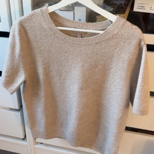 Beige stickad kortärmad tröja H&M - Beige stickad tröja från H&M i storlek S. Tröjan har korta ärmar, rund halsringning och ribbade muddar vid ärmslut och nederkant. Perfekt för lager-på-lager och enkel att matcha med jeans eller kjol.