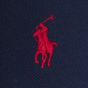 Marinblå pikétröja från Ralph Lauren - Klassisk marinblå pikétröja från Ralph Lauren med den ikoniska röda broderade polospelaren på bröstet. Tröjan är tillverkad i bomull och har en tidlös design som passar perfekt till jeans eller chinos.