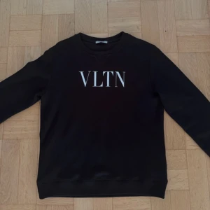 Svart Valentino sweatshirt med VLTN-print - Pris kan diskuteras. Svart äkta sweatshirt från Valentino med stort VLTN-tryck i vitt på bröstet. Klassisk rund hals och ribbade muddar vid ärmslut och nederkant. Långärmad och tillverkad i mjuk bomull, perfekt för dig som gillar stilrena designer och exklusiva märken. 