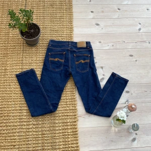 Mörkblå jeans från Nudie Jeans - Snygga mörkblå jeans från Nudie Jeans med klassisk orange söm och ikonisk broderad bakficka. Tillverkade i ekologisk bomull och har en rak passform. Perfekta för dig som gillar stilrena och tidlösa jeans med schyssta detaljer.