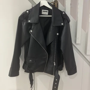 Svart oversized skinnjacka Noisy May - Svart oversized bikerjacka från Noisy May i syntetmaterial med klassiska silvriga dragkedjor, breda slag och bälte i midjan. Skickar gärna passform samt mer bilder om du är intresserad! Vid snabb affär kan jag gå ner i pris! Ordinarie pris 899kr! 