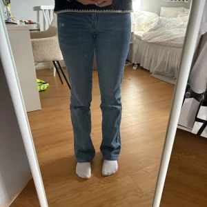 Blå bootcut/raka jeans - Säljer ett par blå jeans med bootcut/ rak passform och låg midja. Snygga slitningar på vänster lår. W26