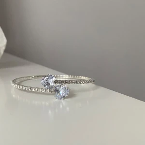 Armband med hjärtformade stenar - Snyggt elegant armband  med  små stenar längs hela bandet och två större hjärtformade, klara stenar framtill. Armbandet är justerbart och ca 18 cm 