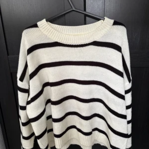 Randig stickad tröja i vitt och svart - Snygg stickad tröja med breda svarta ränder på vit botten. Tröjan har en rund halsringning och avslappnad passform, perfekt för lager på lager. Ribbstickade muddar vid hals, ärmslut och nederkant ger en extra touch.