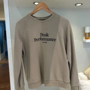 Beige Peak Performance sweatshirt M - Använd väldigt få gånger, som ny. Snygg beige sweatshirt från Peak Performance i storlek M. Tröjan har rund halsringning, svart broderad logga framtill och ribbade muddar vid ärmslut och nederkant. Perfekt för en chill och stilren look. 🥰🥰