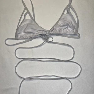 Vit bikini med långa knytband - Supersnygg vit bikini med trekantsmodell och extra långa knytband som kan lindas runt midjan. Sidenliknande material ger en lyxig känsla och den minimalistiska designen gör den perfekt för stranden. Enkel och trendig look som sticker ut.