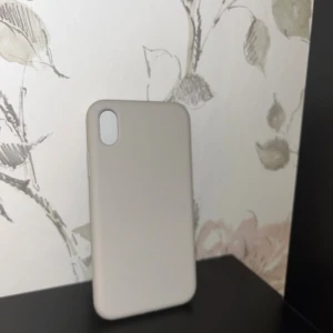 iPhone XR Skal - Elegant och stilrent skal för iPhone XR i ljusgrå/beige färg. Skalet är i gott skick utan synliga repor eller skador. Ger bra skydd mot stötar och repor samtidigt som det är tunt och smidigt. Perfekt för dig som vill skydda din iPhone med en diskret design.
