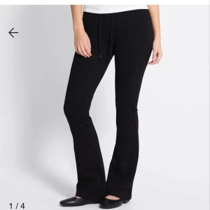 Svarta bootcut mjukisbyxor med snörning - Svarta mjukisbyxor med bootcut-snitt och snörning i midjan. Byxorna har en skön passform och är perfekta för en avslappnad stil. Tillverkade i mjukt material som ger en bekväm känsla hela dagen.