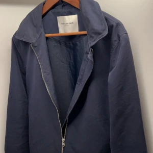 Mörkblå vindjacka från Theory Days - Säljer en stilren mörkblå vindjacka från These glory days. Jackan har klassisk krage, silverfärgad dragkedja och knappar vid ärmsluten. Tillverkad i bomullsmix och har en clean, minimalistisk look som passar perfekt till vad som helst. Nypris på cirka 1500kr! Modellen är 187